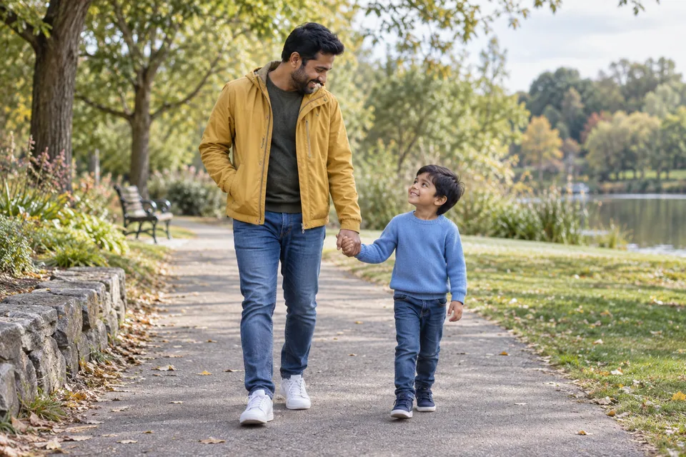 Ein Vater in senffarbener Jacke und sein kleiner Sohn halten sich auf einem Parkweg an der Hand.